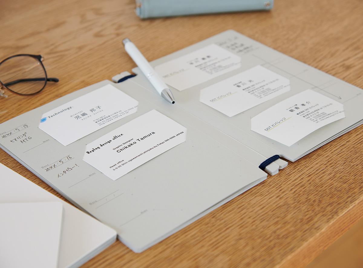 名刺と手書きメモを収納したLog bookが机に開かれている様子